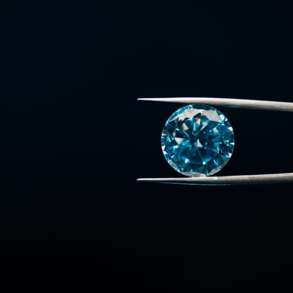 colorful blue sparkling diamond in tweezers isolated on black