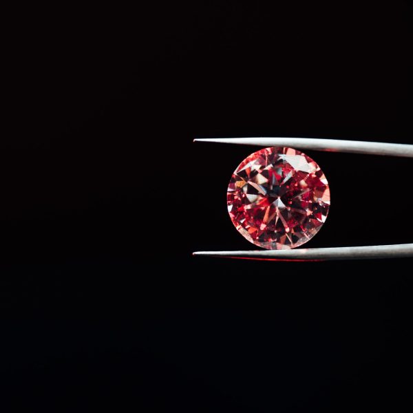 colorful red sparkling diamond in tweezers isolated on black