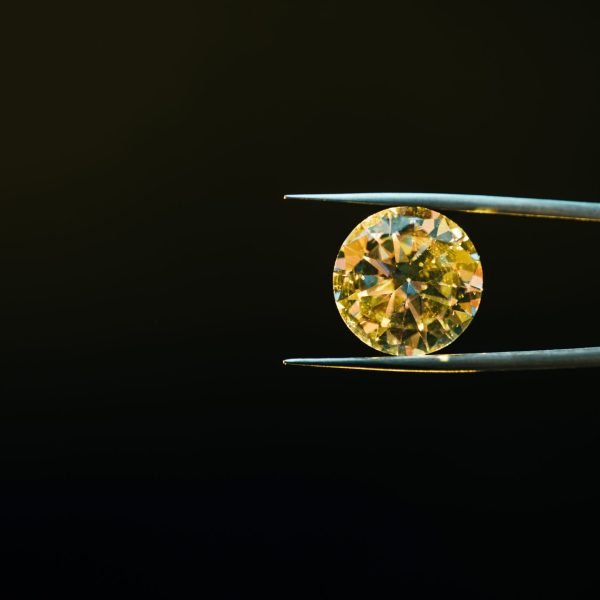 colorful yellow sparkling diamond in tweezers isolated on black